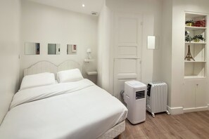 A bedroom with a bed, bedside tables, a heater, a wardrobe, and a shelf with decorative items. - Madeleine Flat - One Bedroom Apartment, Sleeps 4 (Paris)