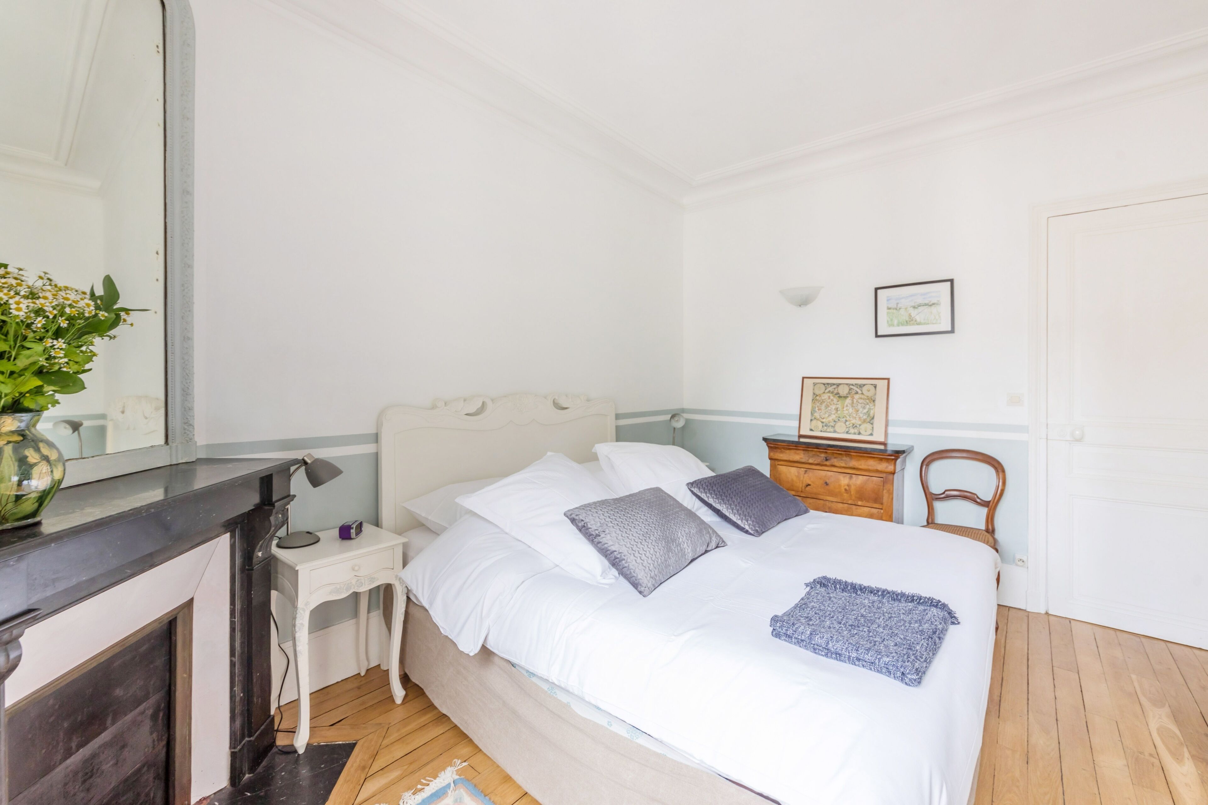 Une chambre à coucher comprenant un lit, une table de chevet, une lampe, une commode, une chaise et un miroir.