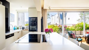 Eine moderne Küche mit Kochinsel, einem Essbereich mit Stühlen und Blick auf einen Balkon mit Pflanzen.