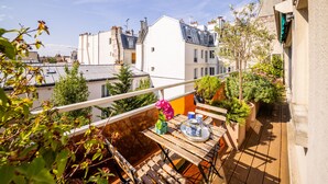Ein Balkon mit Holztisch, Blumentöpfen und einem Blumenstrauß.