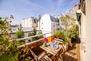 A balcony with a wooden table, potted plants, and a vase of flowers. - Montmartre Luminous - One Bedroom Apartment, Sleeps 3 (Paris)