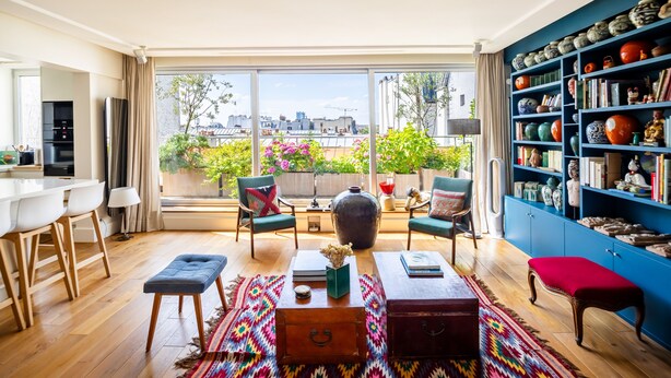 Ein modernes Wohnzimmer mit Balkon, Holzboden, Essbereich und einem blauen Bücherregal.