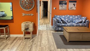 A living room with a wooden coffee table, a blue sofa with sailboat patterns, and a wall clock. - updated 2-bedroom, 2 bath, sleeps 6 family friendly condo. Many extras. (Gulf Shores)