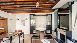 A modern interior with a wooden ceiling, a dining table with chairs, a fireplace, and a sofa in the background. - Île Saint Louis Cosy (Paris)