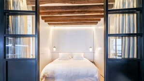 A modern bedroom with a large bed, wooden ceiling beams, and a large mirror. - Île Saint Louis Cosy (Paris)