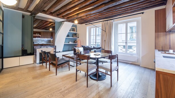A modern kitchen with wooden beams, a dining area with chairs and a table, and a view through a window. - Île Saint Louis Cosy (Paris)