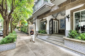 Un bâtiment à la façade de style traditionnel, avec des marches menant à une porte et un trottoir bordé d’arbres.