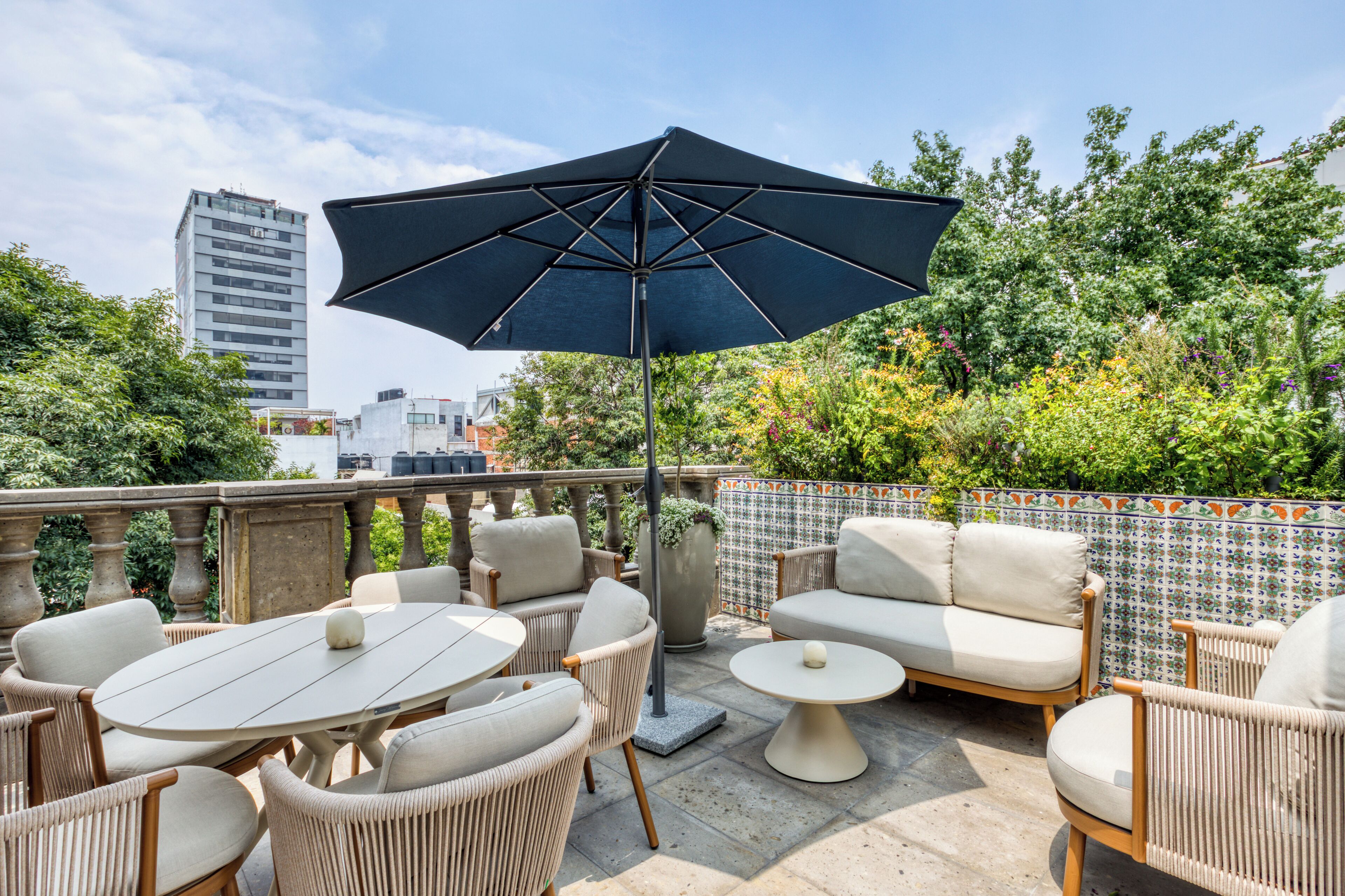 A rooftop terrace with outdoor furniture, a large umbrella, and a view of a cityscape.