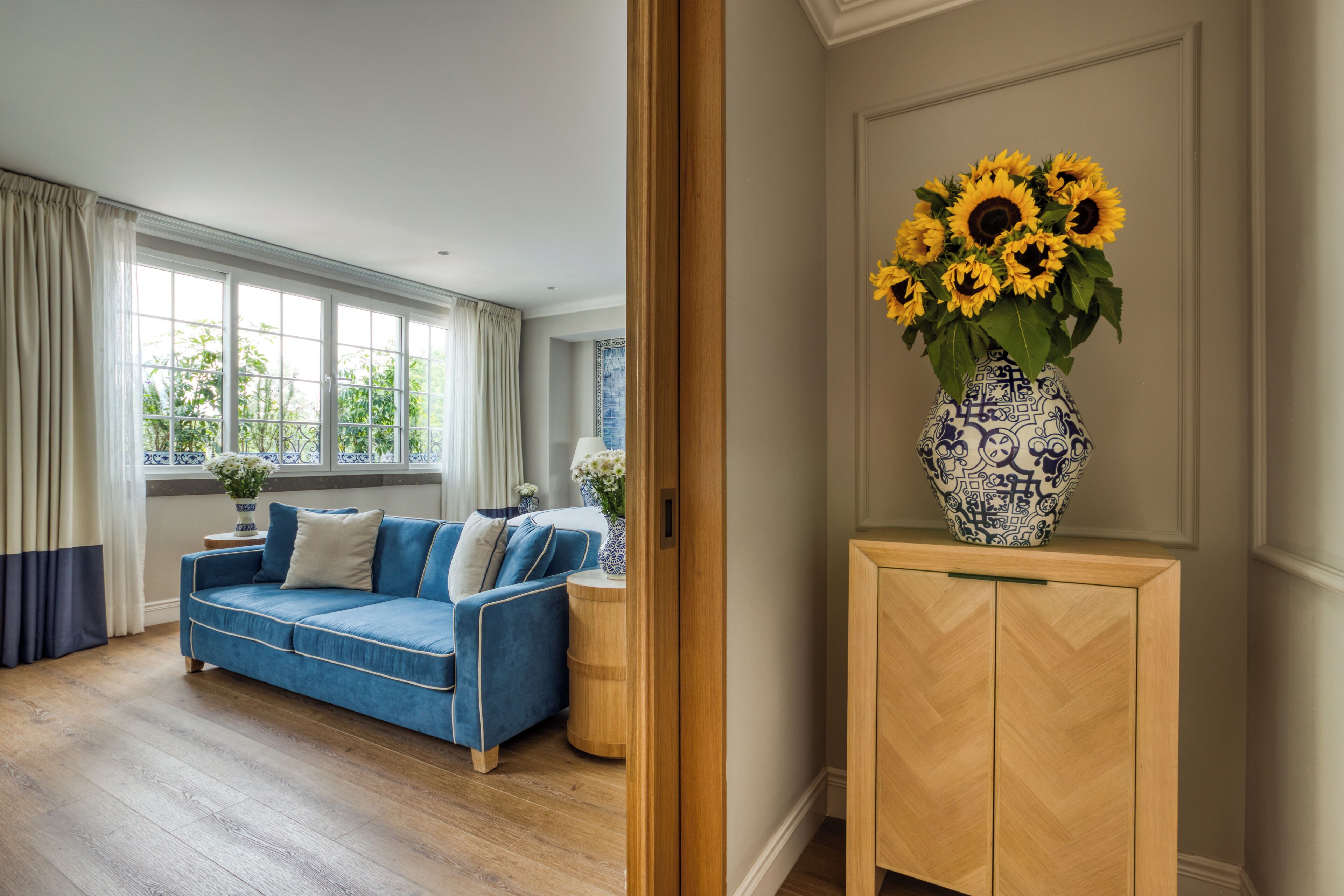 A room with a blue sofa, a wooden cabinet, and a vase with sunflowers.