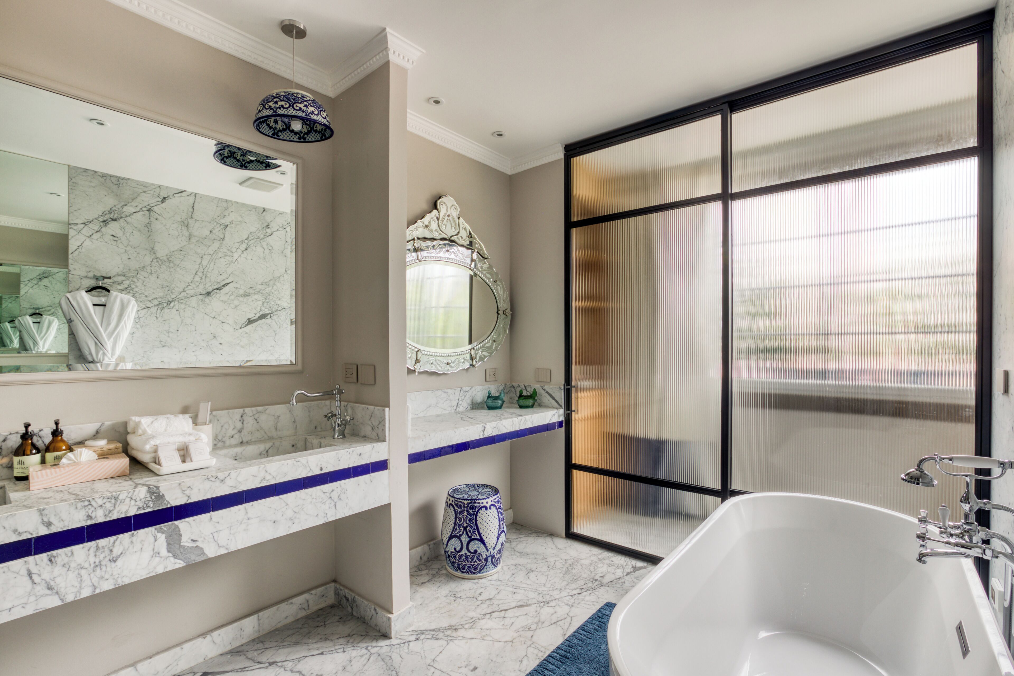 Une salle de bain moderne avec un grand miroir, des comptoirs en marbre, une baignoire sur pieds et une grande fenêtre offrant une vue dégagée.