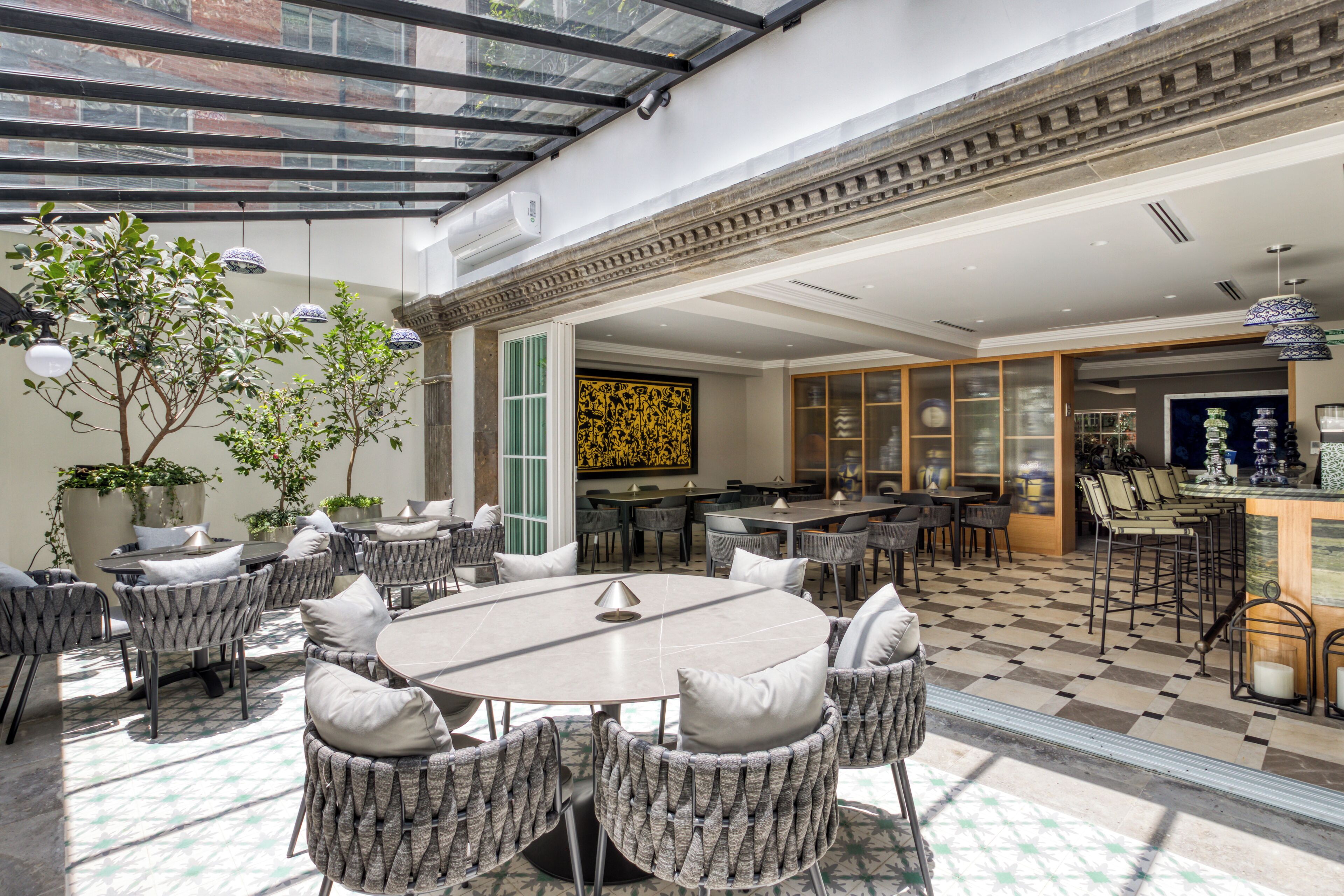 A spacious outdoor dining area with wicker furniture and a central table, surrounded by potted plants and a checkered floor pattern.