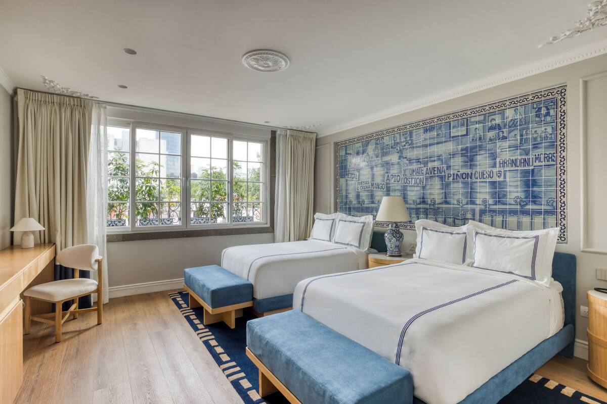 Une chambre d’hôtel avec deux lits, un bureau, une chaise et une grande fenêtre avec des rideaux.