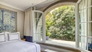 A hotel room with a large bed, a window with a view of greenery, and a decorative wall piece. - Casa Talavera by Tasman (Mexico City)