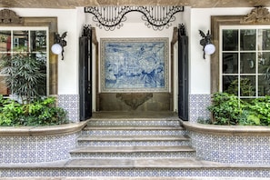 A building entrance with a tiled floor, a large blue and white tiled wall, and a decorative metal railing above the steps. - Casa Talavera by Tasman (Mexico City)