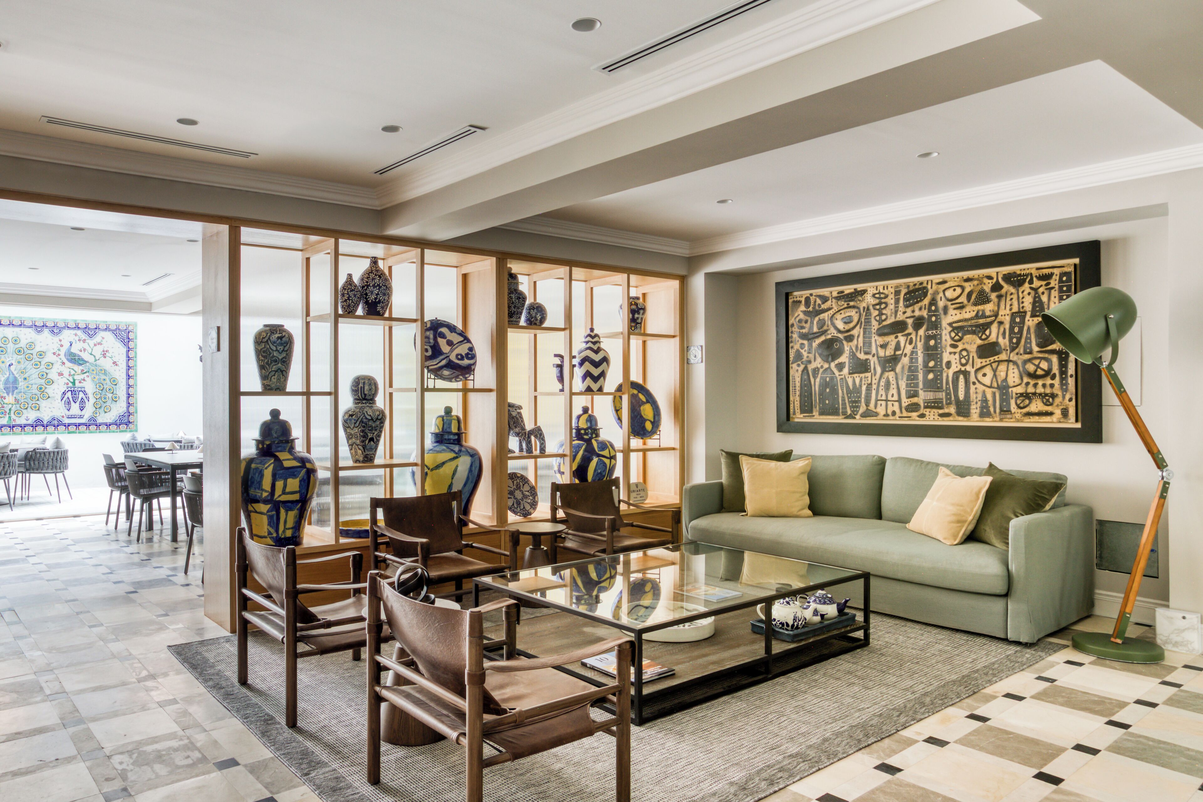 A living room with a sofa, chairs, a coffee table, a glass display case with vases, and a large framed artwork on the wall.