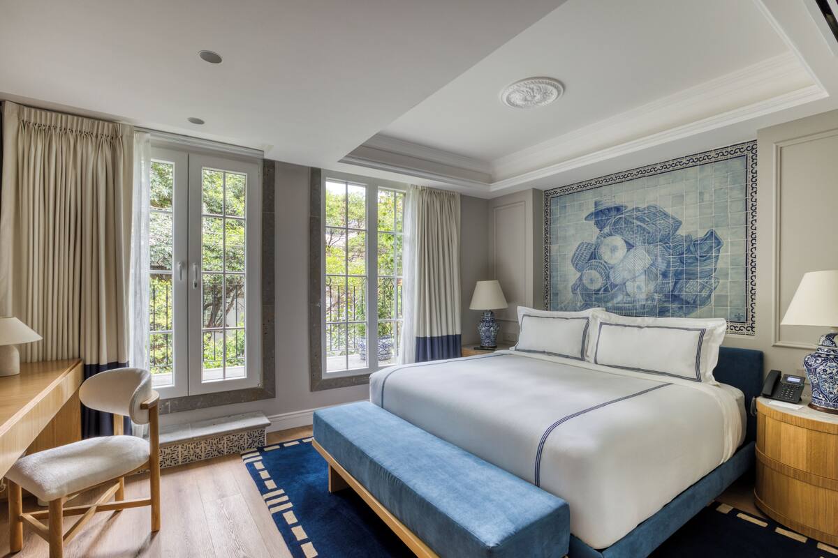 Une chambre à coucher avec un grand lit, un bureau, une chaise et une fenêtre avec des rideaux.