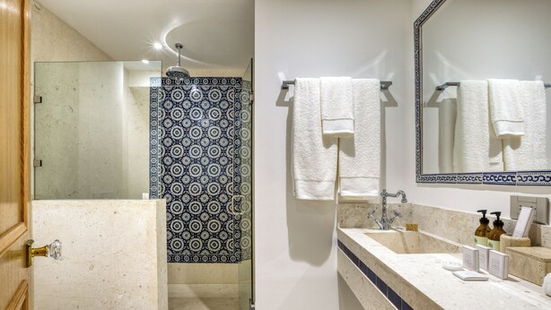A bathroom with a glass shower enclosure, a white toilet, a sink with a marble countertop, and a large mirror. - Casa Talavera by Tasman (Mexico City)