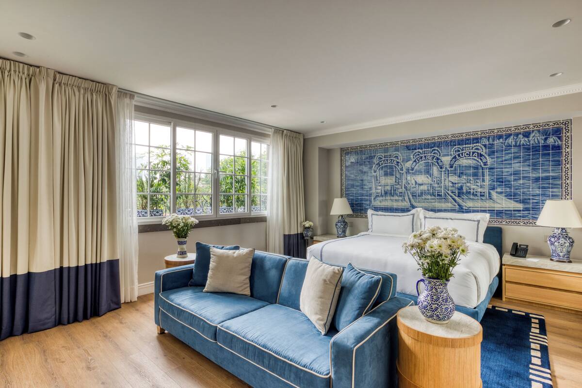 Une chambre à coucher avec un lit, un canapé bleu, une table de chevet en bois et un mur recouvert de carreaux bleus et blancs.