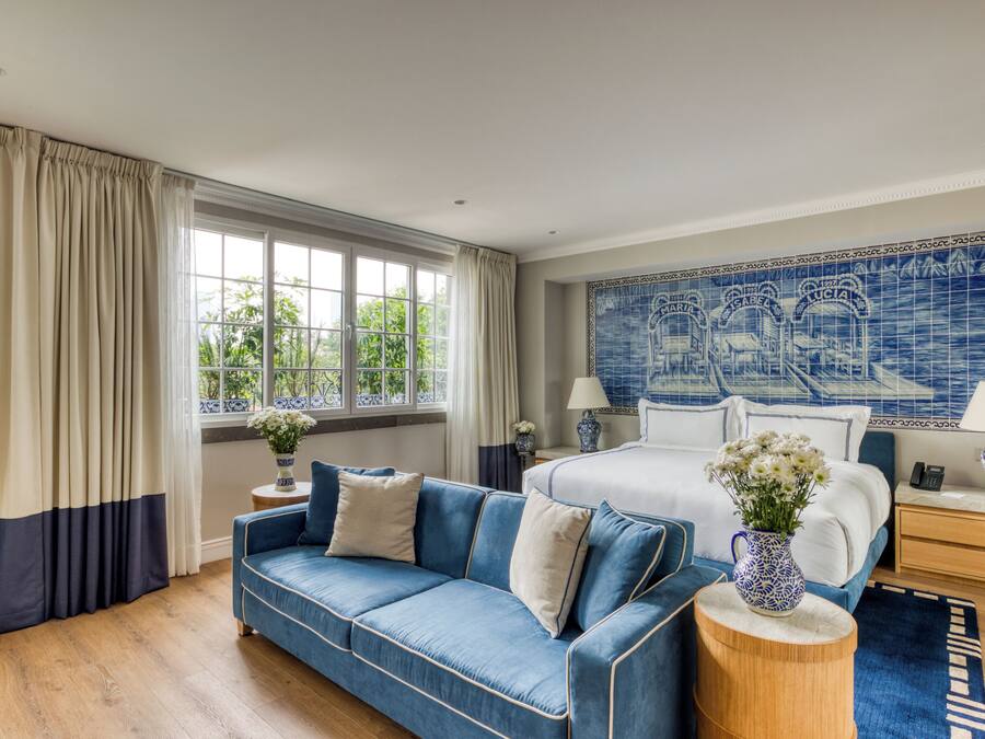 Un dormitorio con cama, un sofá azul, una mesita de noche de madera y una pared con azulejos azules y blancos.