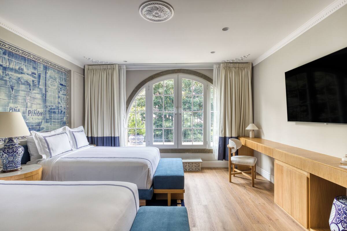 Une chambre d’hôtel avec deux lits, un bureau, une télévision et une grande fenêtre avec des rideaux.