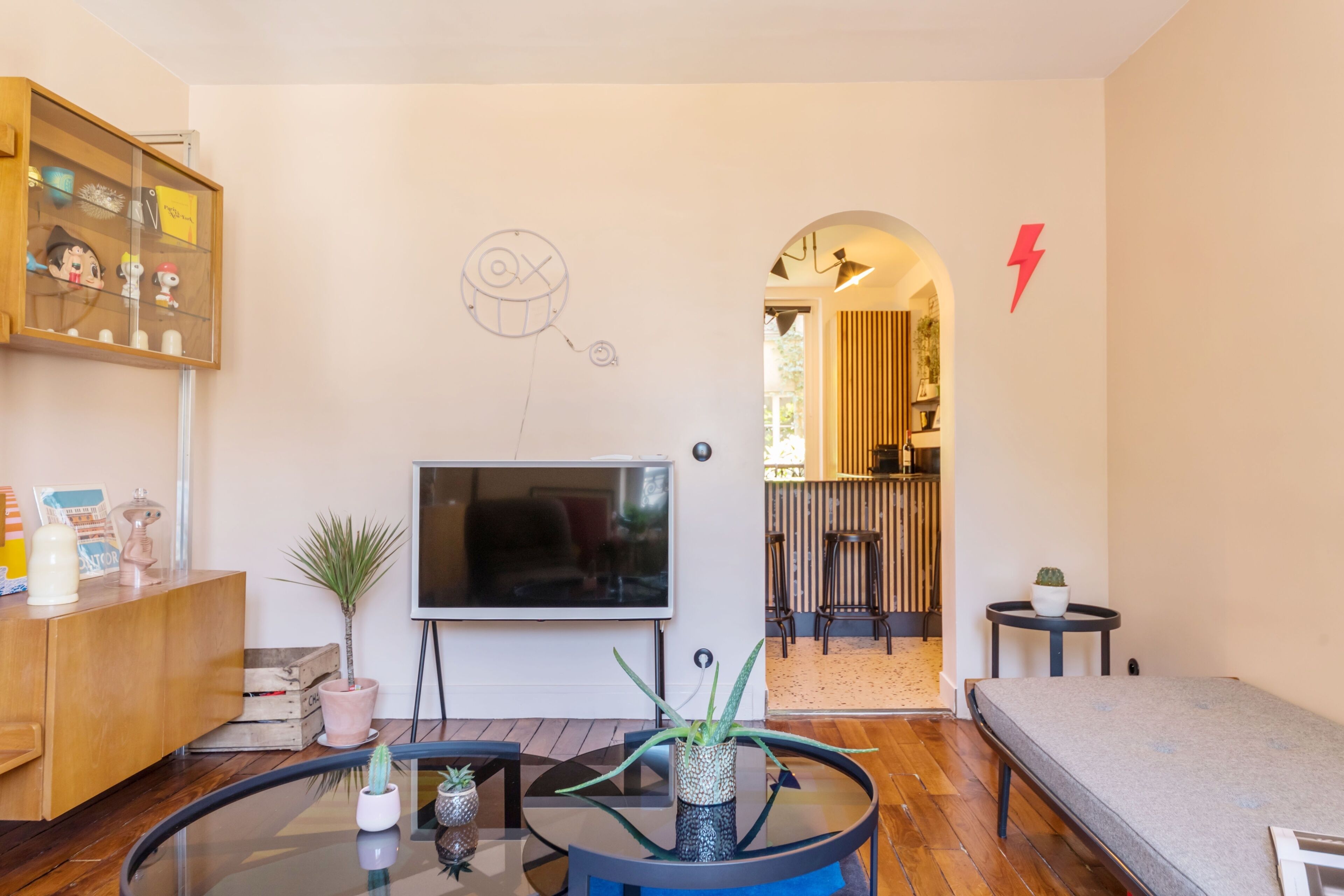 Una sala de estar con televisor, una mesa de centro de vidrio, sofá, aparador de madera y una pequeña planta en maceta.