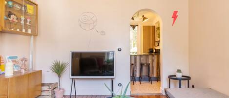 Una sala de estar con televisor, una mesa de centro de vidrio, sofá, aparador de madera y una pequeña planta en maceta.