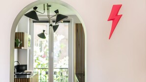 An arched mirror reflecting a kitchen area with a modern chandelier, a red lightning bolt decoration, and a view of greenery outside. - Canal St Martin Valmy (Paris)