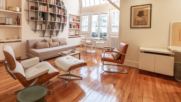 Un salon moderne comprenant un canapé, des fauteuils, une table basse, une bibliothèque et un coin repas avec des chaises et une table.