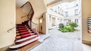 Un carrer estret amb una escala que condueix a la façana d'un edifici, una petita zona verda i balcons amb finestres.