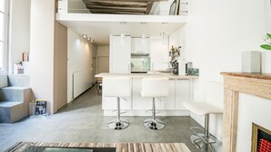 Una cuina moderna amb una illa central, tamboretes blancs i un sostre de fusta.