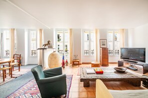 A living room with a TV, a sofa, a coffee table, and a dining area with chairs and a table. - Montmartre Martyrs - One Bedroom Apartment, Sleeps 2 (Paris)