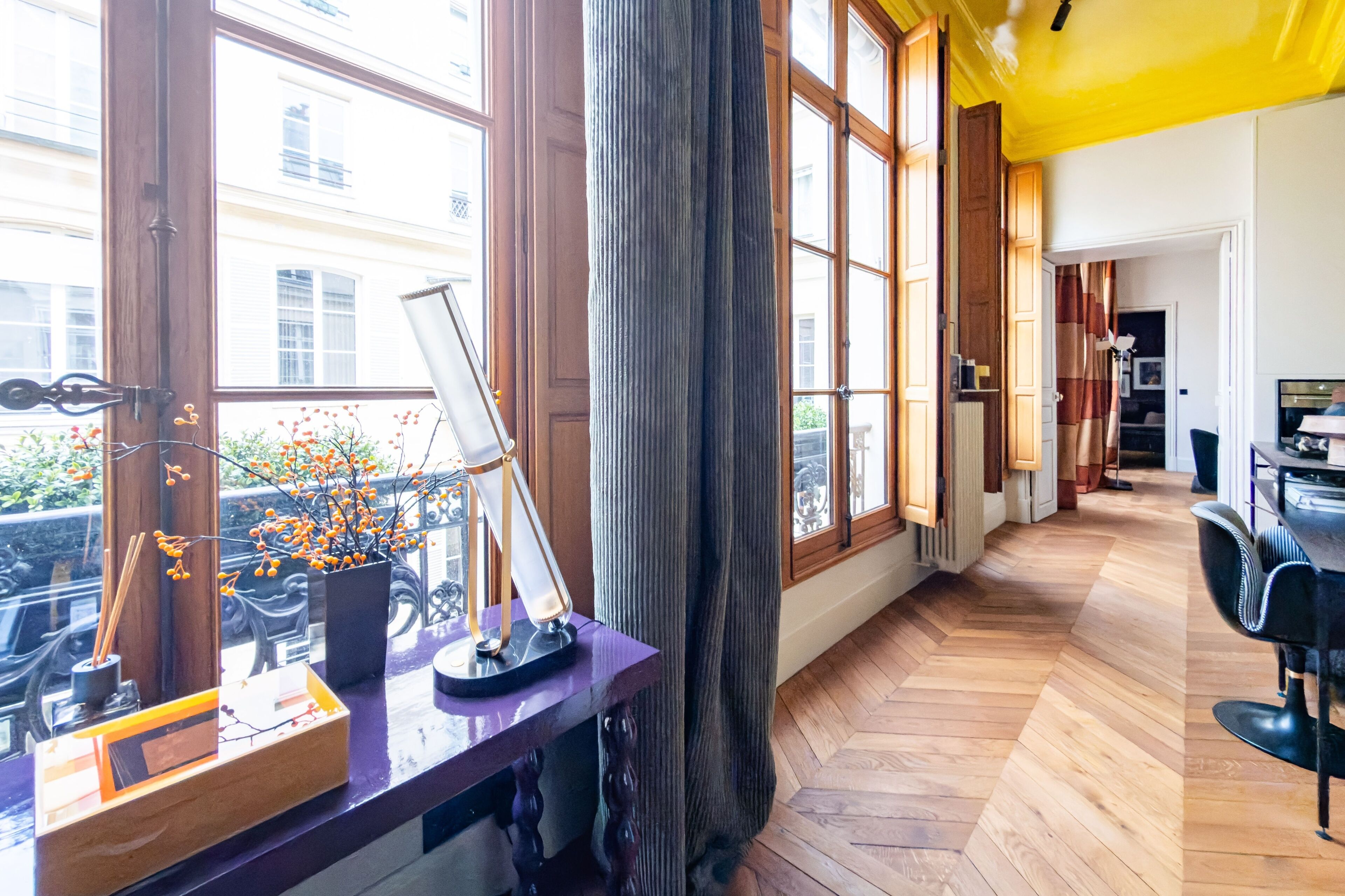 Une pièce avec de grandes fenêtres, un plancher en bois, un bureau avec une lampe et une chaise.