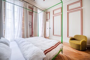 Ein Schlafzimmer mit einem Bett, einem Sessel und einem Fenster mit Vorhängen.