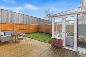 A backyard with a wooden deck, a glass-enclosed patio, and a fenced area. - NEW! Stylish 3-Storey Townhouse | Free Parking (Bromborough)