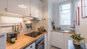 Une cuisine moderne avec des armoires blanches, un plan de travail en bois, un four encastré et une fenêtre laissant entrer la lumière naturelle.