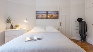 Une chambre à coucher avec un lit, une table de chevet avec une lampe, une plante et deux tableaux encadrés accrochés au mur.