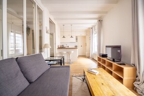 Ein modernes Wohnzimmer mit grauem Sofa, Couchtisch aus Holz und einem Fernseher auf einem Standfuß.
