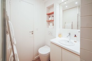 Ein Badezimmer mit Toilette, Waschbecken, Spiegel und Ablagen für Pflegeprodukte.