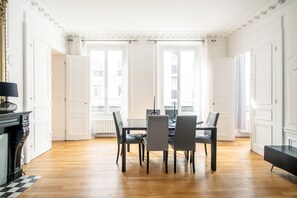 A dining area with a table and chairs, a fireplace, and large windows with curtains. - Grands Boulevards Family (Paris)