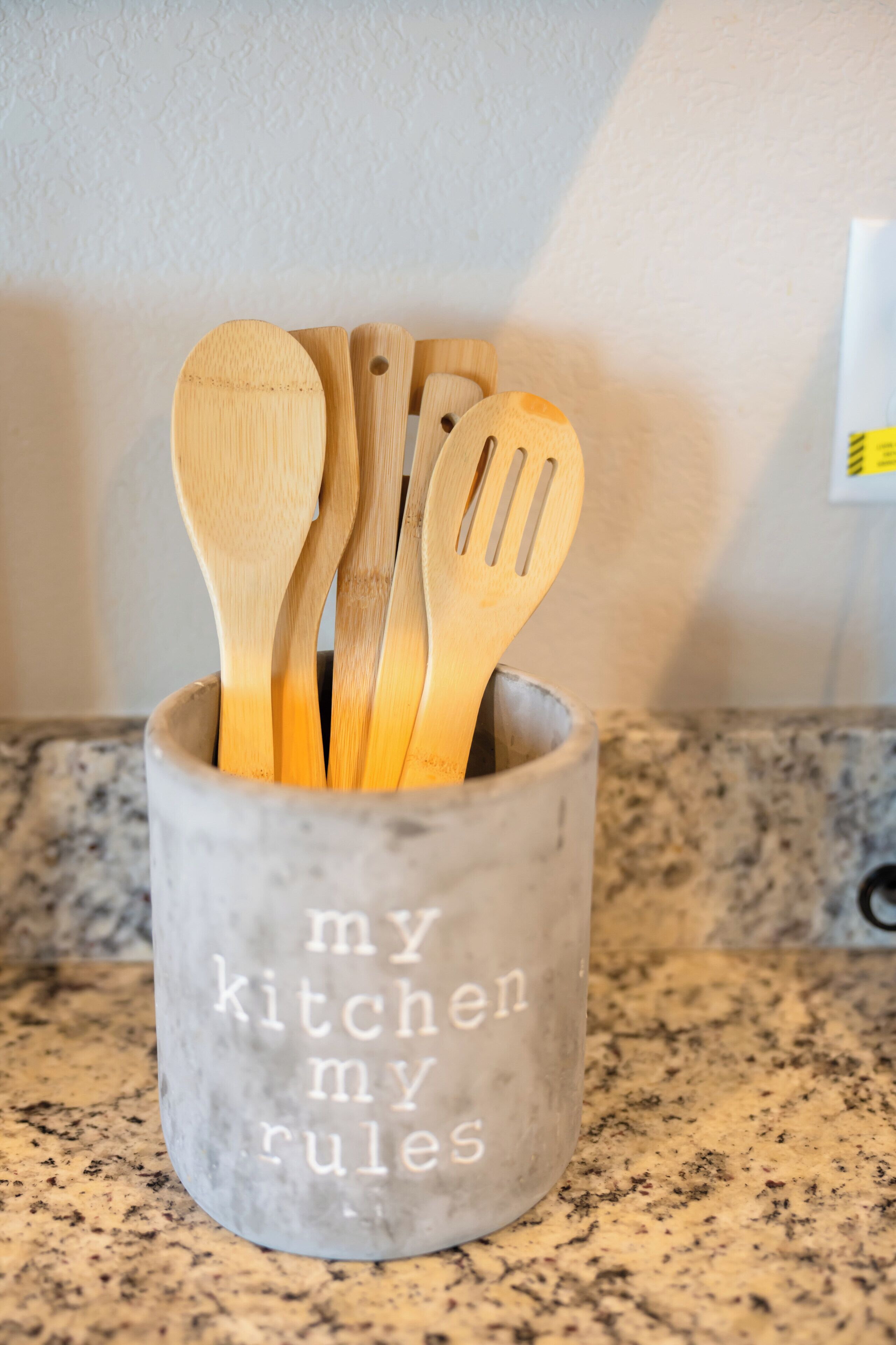 Un porte-ustensiles de cuisine contenant des cuillères en bois et une spatule, avec l’inscription « ma cuisine, mes règles ».