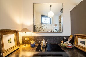 A kitchen with a stove, a mirror, framed pictures, and a lamp. - Marais Enfants Rouges (Paris)