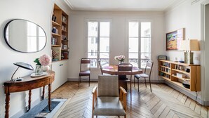 Ein Zimmer mit Esstisch, Stühlen, Bücherregal, Spiegel und Fenster.