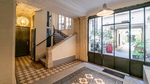 Eine Treppe mit Schachbrettmuster führt zu einer Tür, ein großes Fenster bietet einen Ausblick nach draußen und eine Hängelampe.