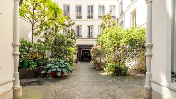 Ein schmaler Innenhof mit einem Kopfsteinpflasterweg, umgeben von Gebäuden mit großen Fenstern und Balkonen.
