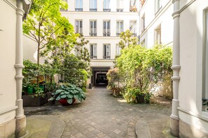 A narrow courtyard with a cobblestone path, surrounded by buildings with large windows and balconies. - Opera Home - Two Bedroom Apartment, Sleeps 4 (Paris)