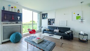 A modern living room with a sofa, a coffee table, a red chair, a blue bean bag, and a TV on a wall. - Buttes Chaumont Botzaris View (Paris)