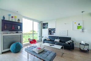 A modern living room with a sofa, a coffee table, a red chair, a blue bean bag, and a TV on a wall. - Buttes Chaumont Botzaris View (Paris)