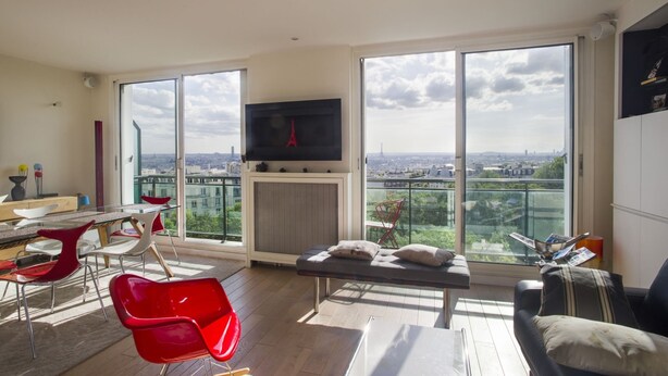 A modern living room with a large TV, a dining area, and a balcony with a city view. - Buttes Chaumont Botzaris View (Paris)