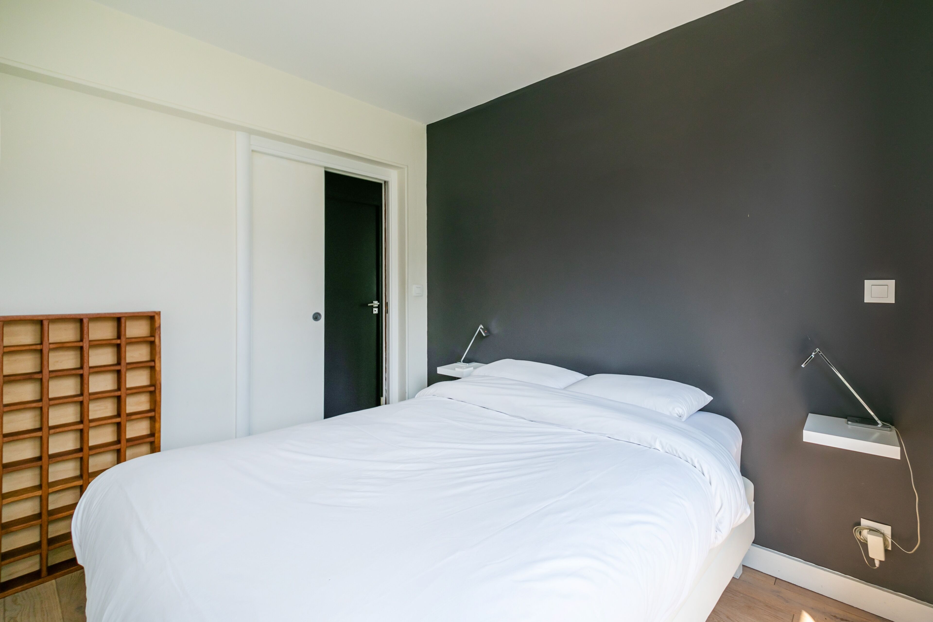 A bedroom with a bed, a wooden headboard, a door, and a wall-mounted light fixture.