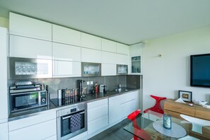 A modern kitchen with stainless steel appliances, white cabinetry, and a glass dining table. - Buttes Chaumont Botzaris View (Paris)